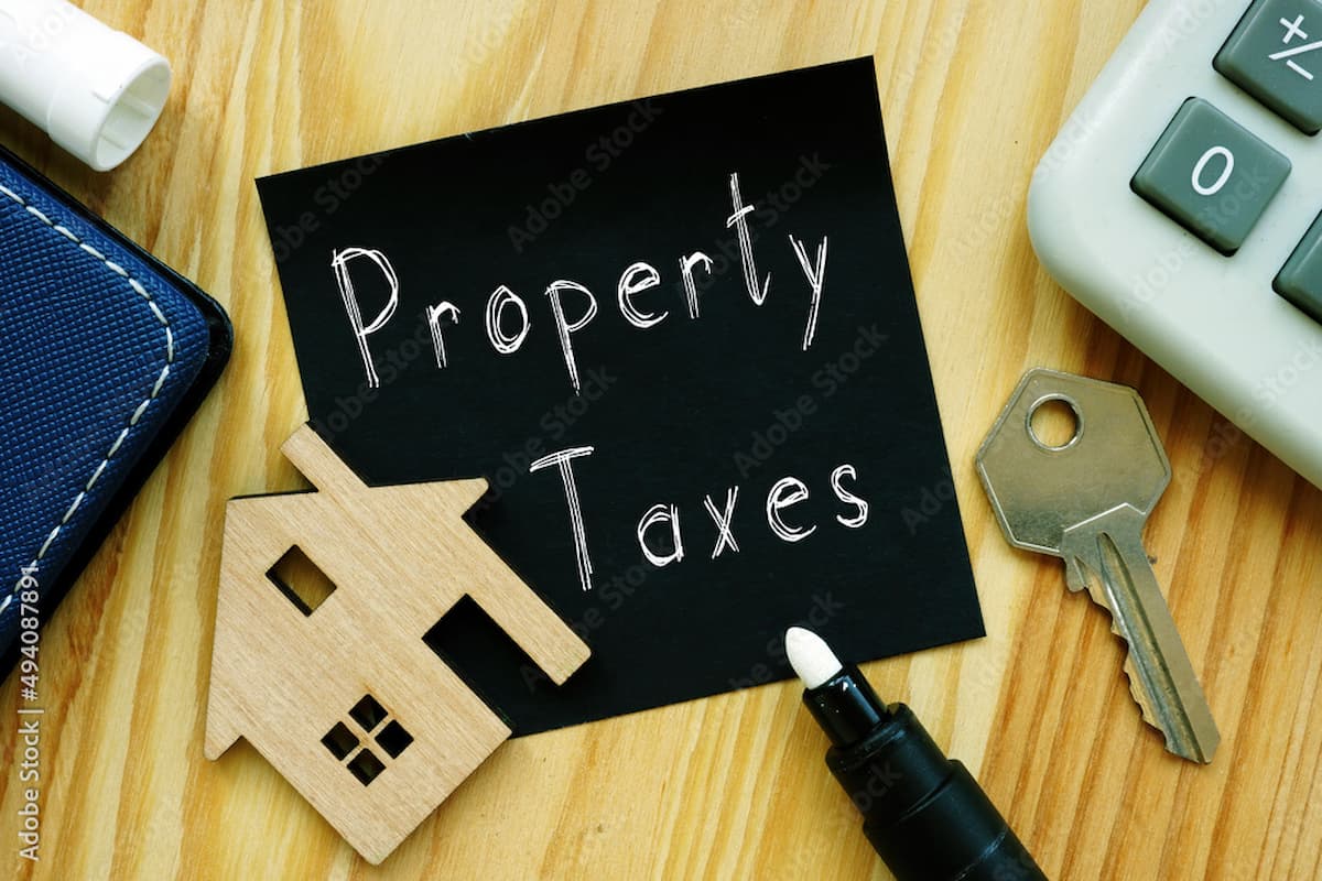 Property Taxes written on a sign near a wooden house, key, and calculator