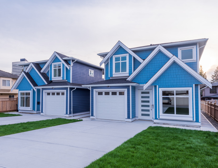 Two blue cottage style production homes, each with sloped roofs, windows and single car garage and driveway
