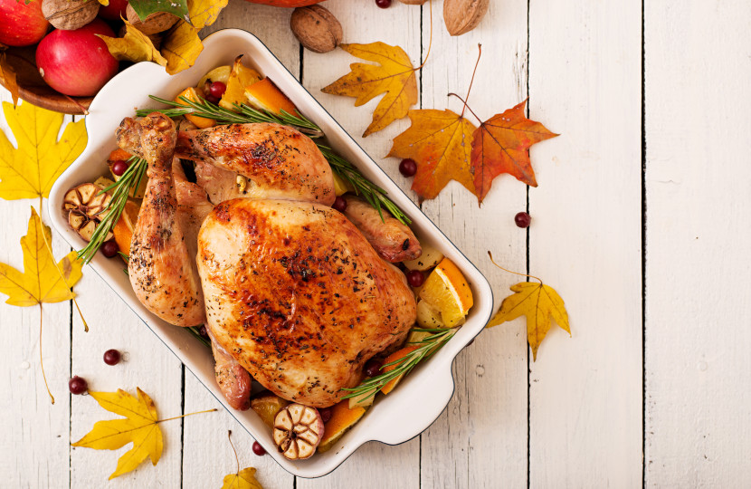 A roast turkey in a white serving dish, with fall leaves on a white table