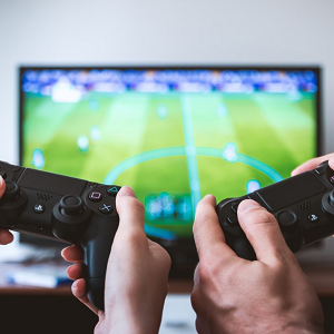 Are video games making your energy bills rocket? Two PS4 video game controllers being held and playing a football game on TV.