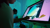 Closeup of young visitor making a collage on an interactive touch screen in The Studio experience.