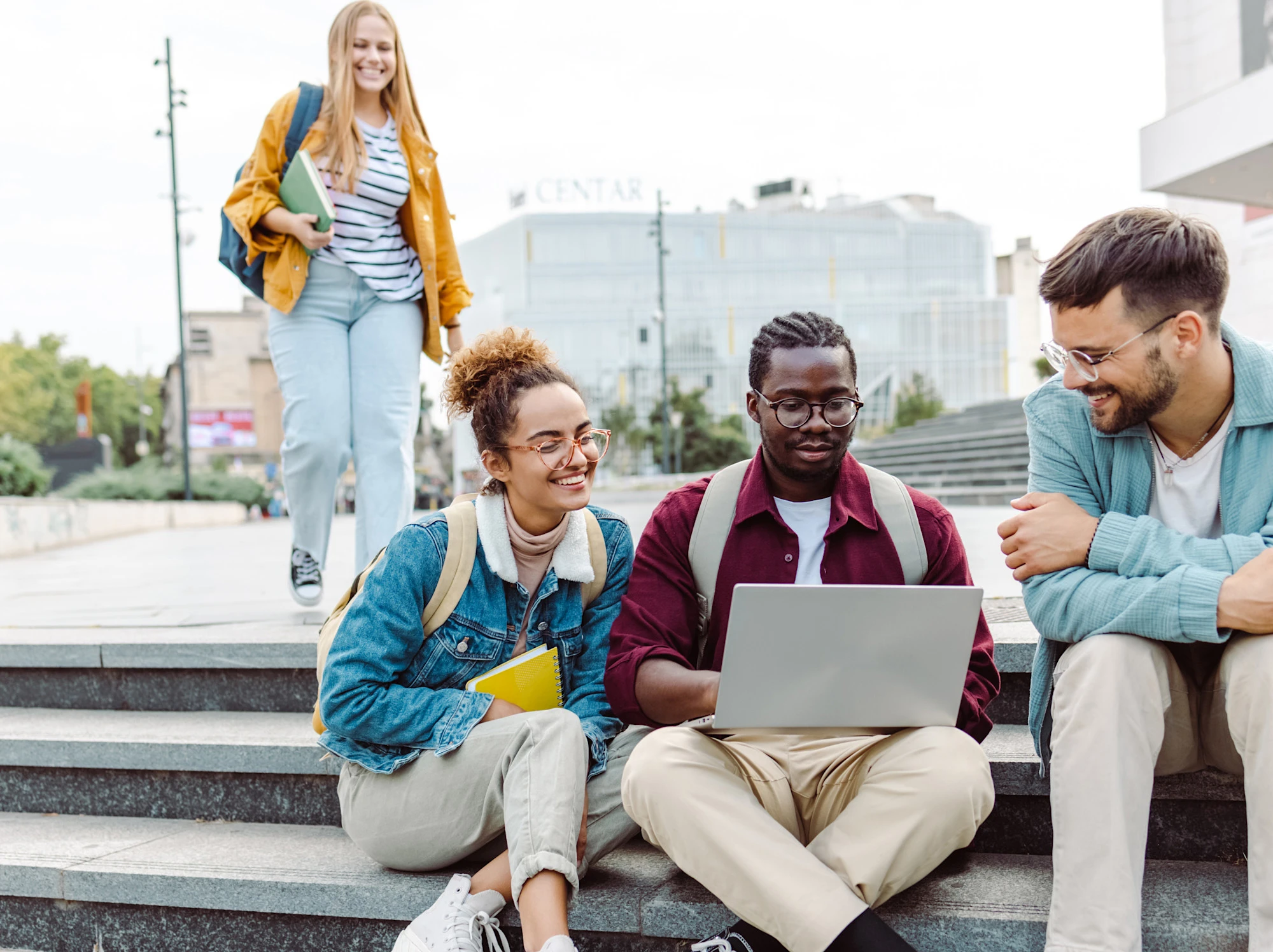 Smiling students studying together, sitting on steps outside their school.