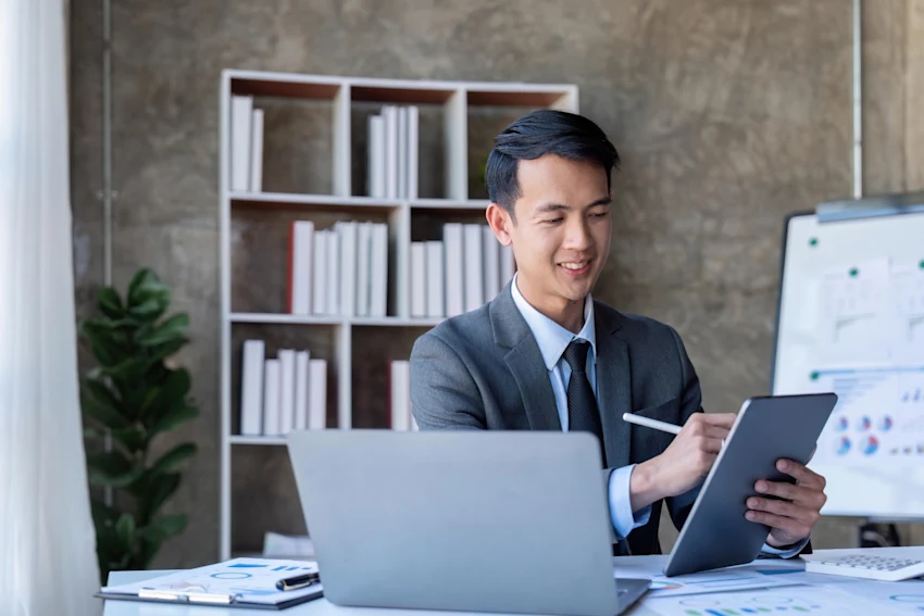 Professional man studying for the CFA exam using a tablet and laptop in a modern office setting