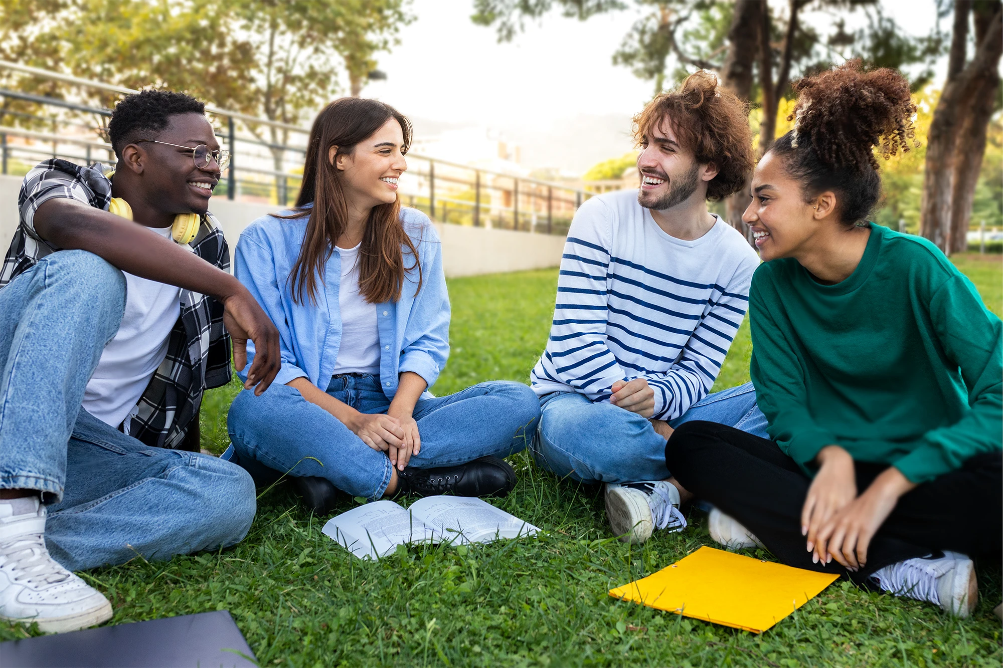Four students sitting on the grass outdoors, smiling and talking