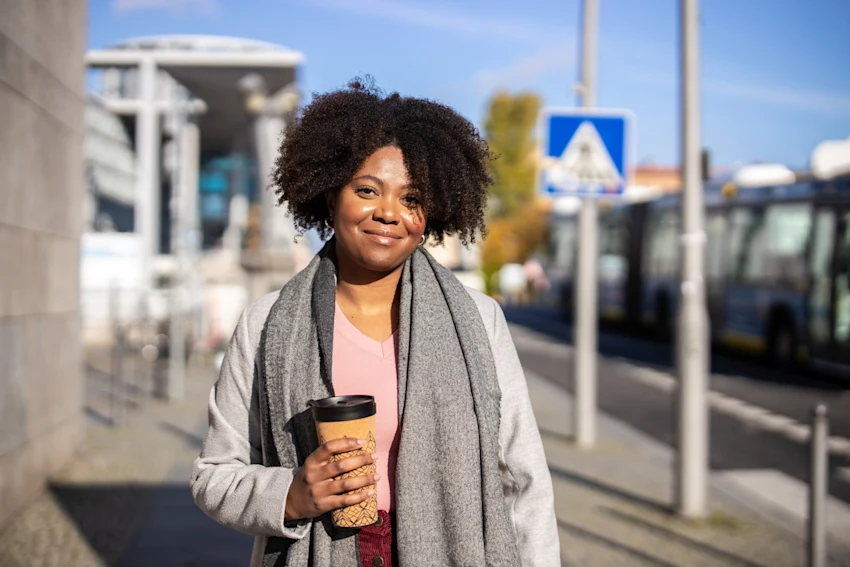 Smiling woman with a coffee cup in hand standing outdoors