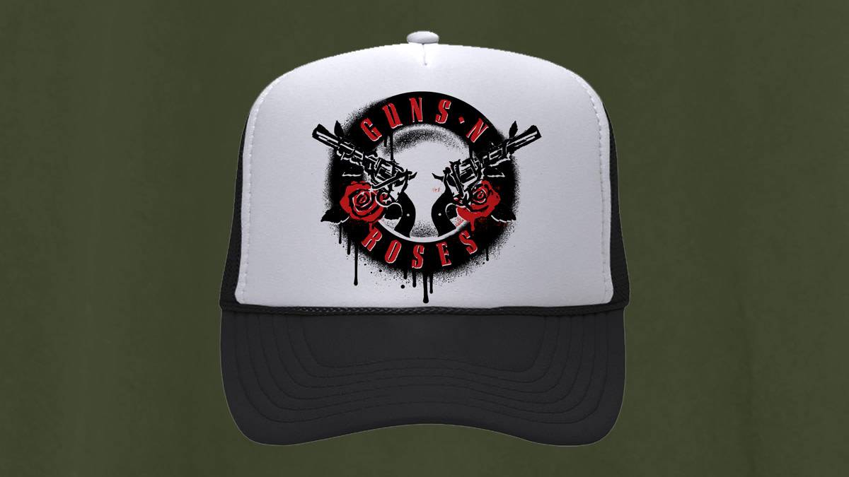 Black and white Guns N’ Roses trucker cap featuring a graphic design with a skull, two revolvers and red roses on the front. The band's name appears in red lettering around the logo. The cap is shown against a blurred green and black background.