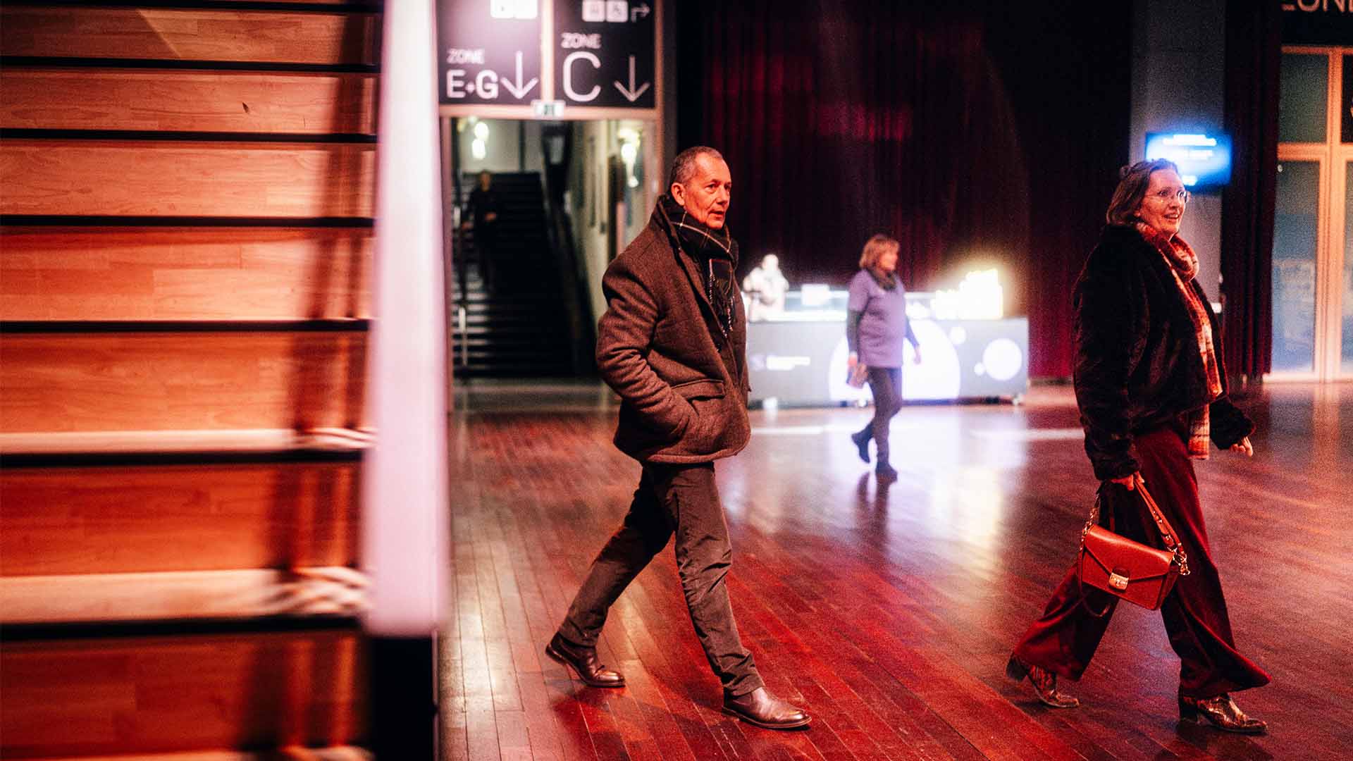 Bezoekers wandelen door de foyer van Stadsschouwburg Antwerpen. Op de achtergrond is een foodstand zichtbaar, samen met een trap naar de zaal.