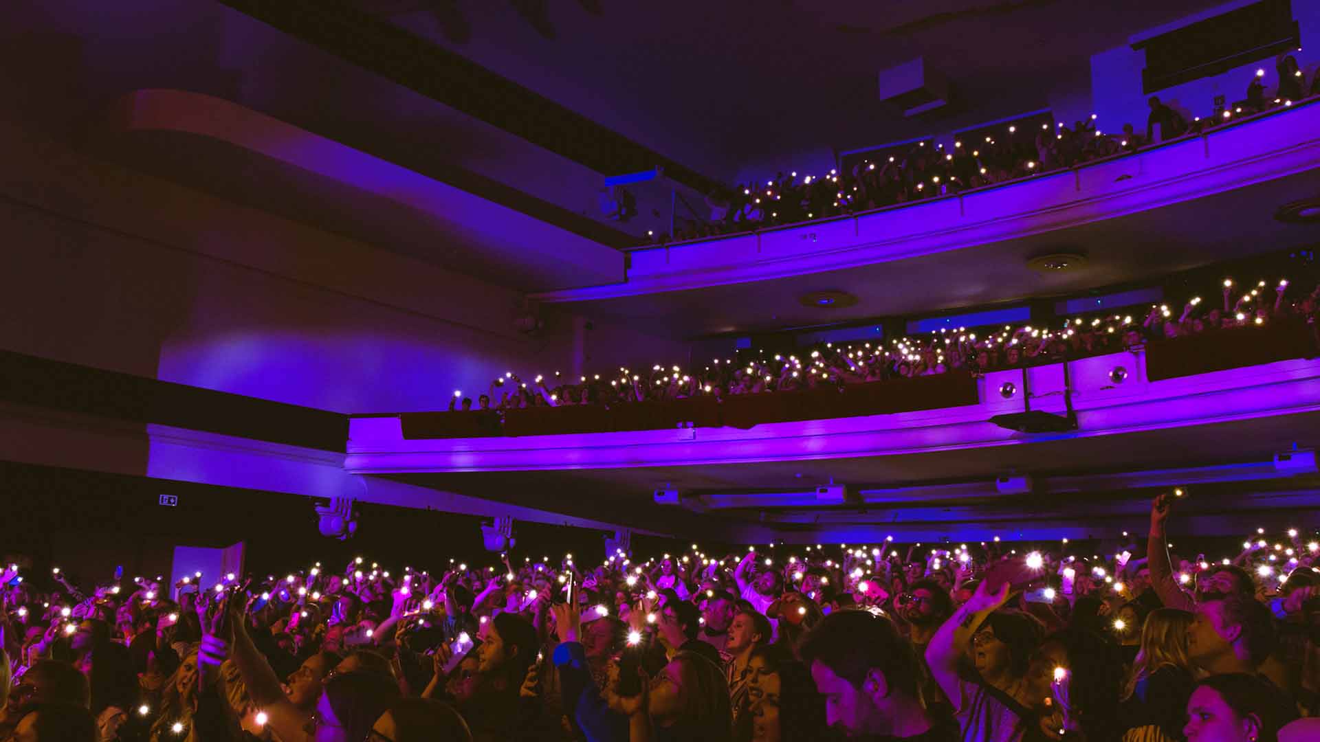 In de zaal is het donker. Op de parterre en in de balkons houden veel fans een lichtje in de lucht.