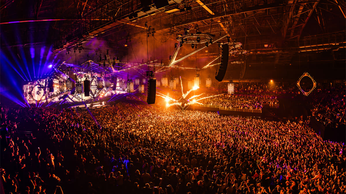 Een uitzinnige mensenmassa geniet van Reverze 2026 in de AFAS Dome, met een indrukwekkende lichtshow, vuurwerk en spectaculaire podiumconstructies.