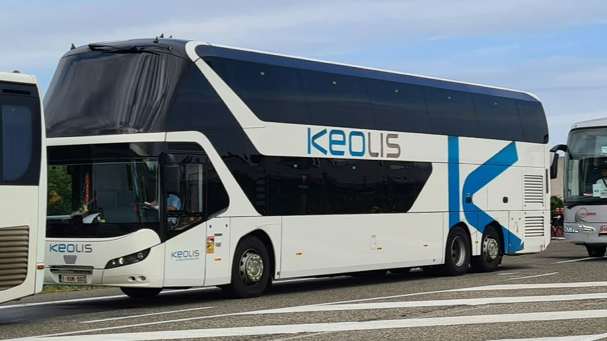 Autocar à deux étages de Keolis, blanc avec des accents bleus, garé sur une route à côté d’autres bus.
