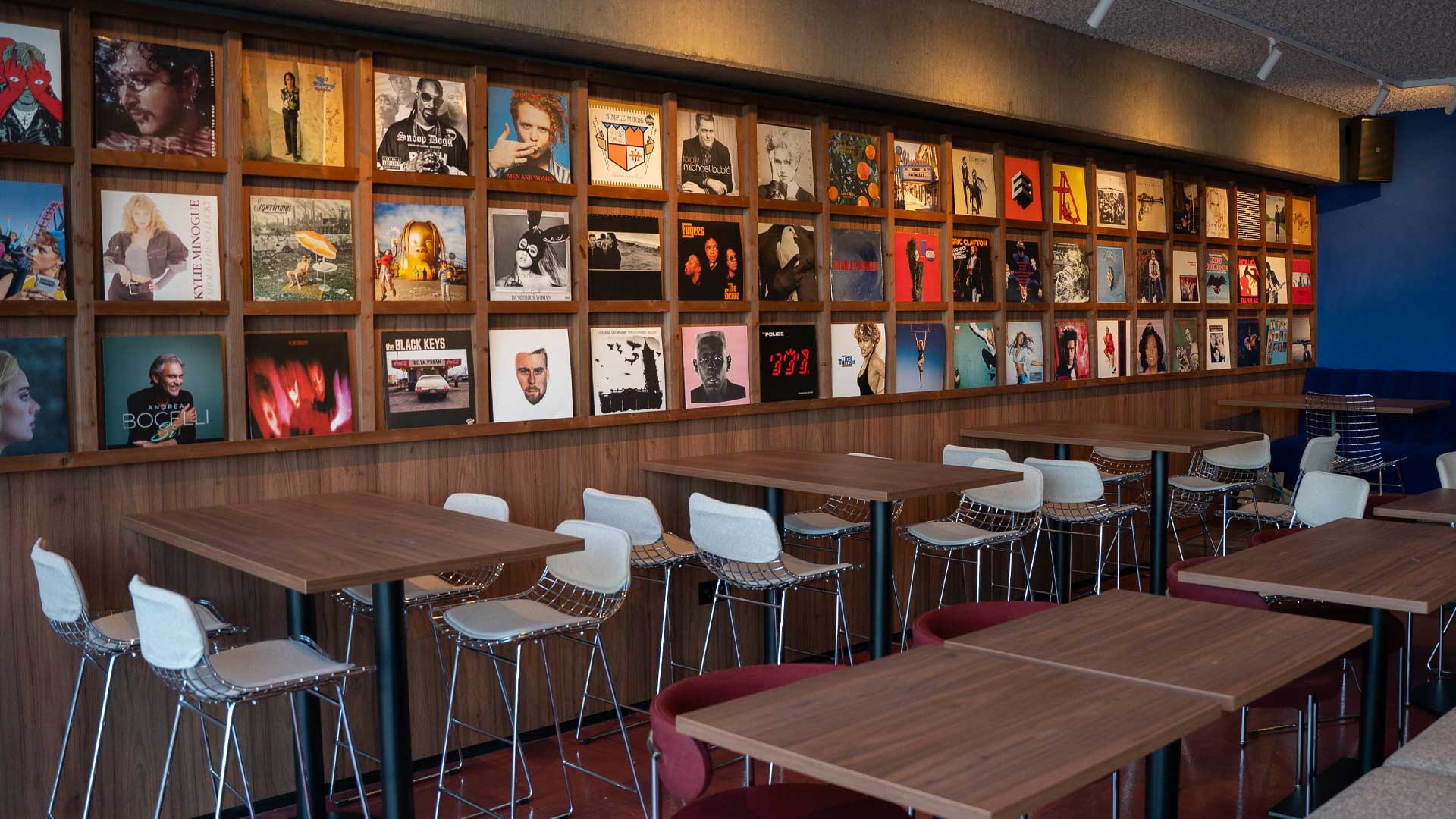 Interior of the AFAS Lounge in the AFAS Dome featuring tables and chairs, with a wall display of album covers by artists and bands.