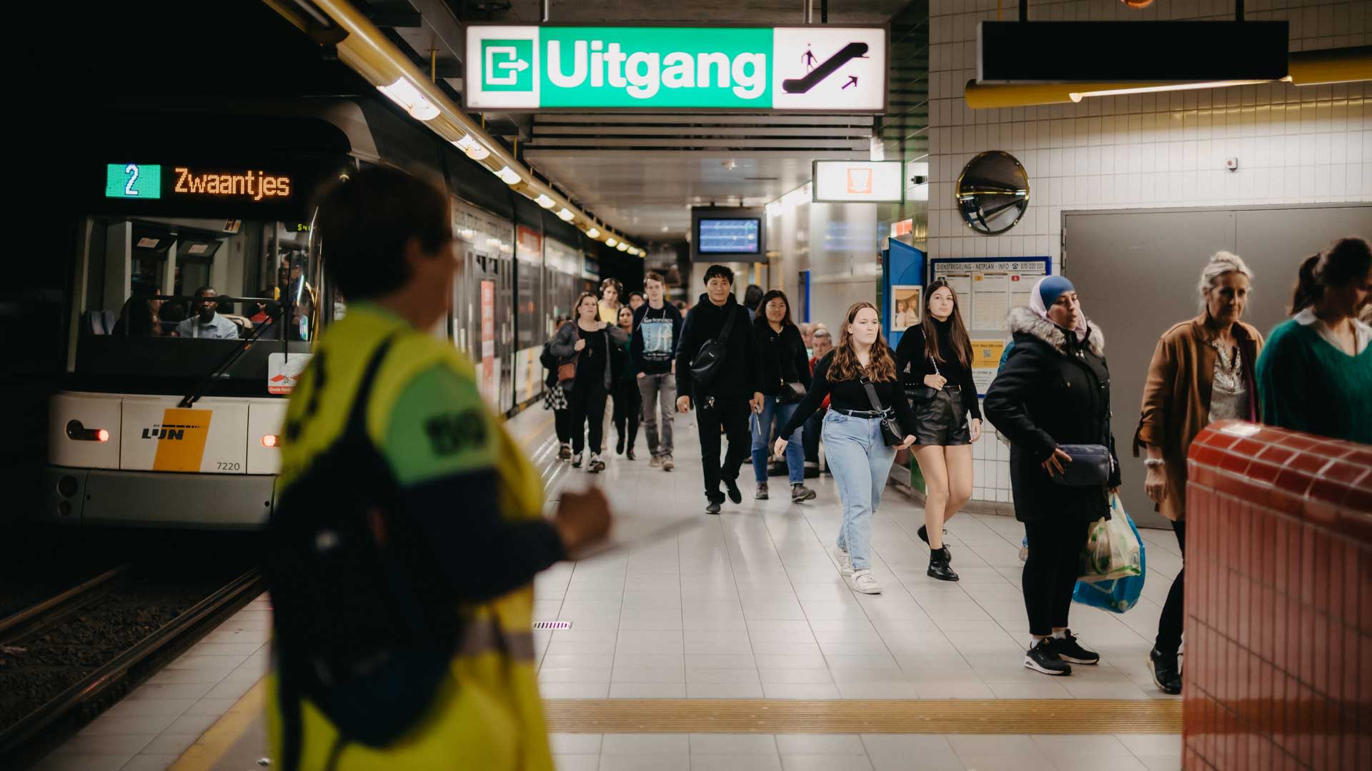 Station de métro Sport à Anvers, à côté de l’AFAS Dome et du Lotto Arena, avec une rame à quai, un panneau « Sortie » et des voyageurs marchant le long du quai.