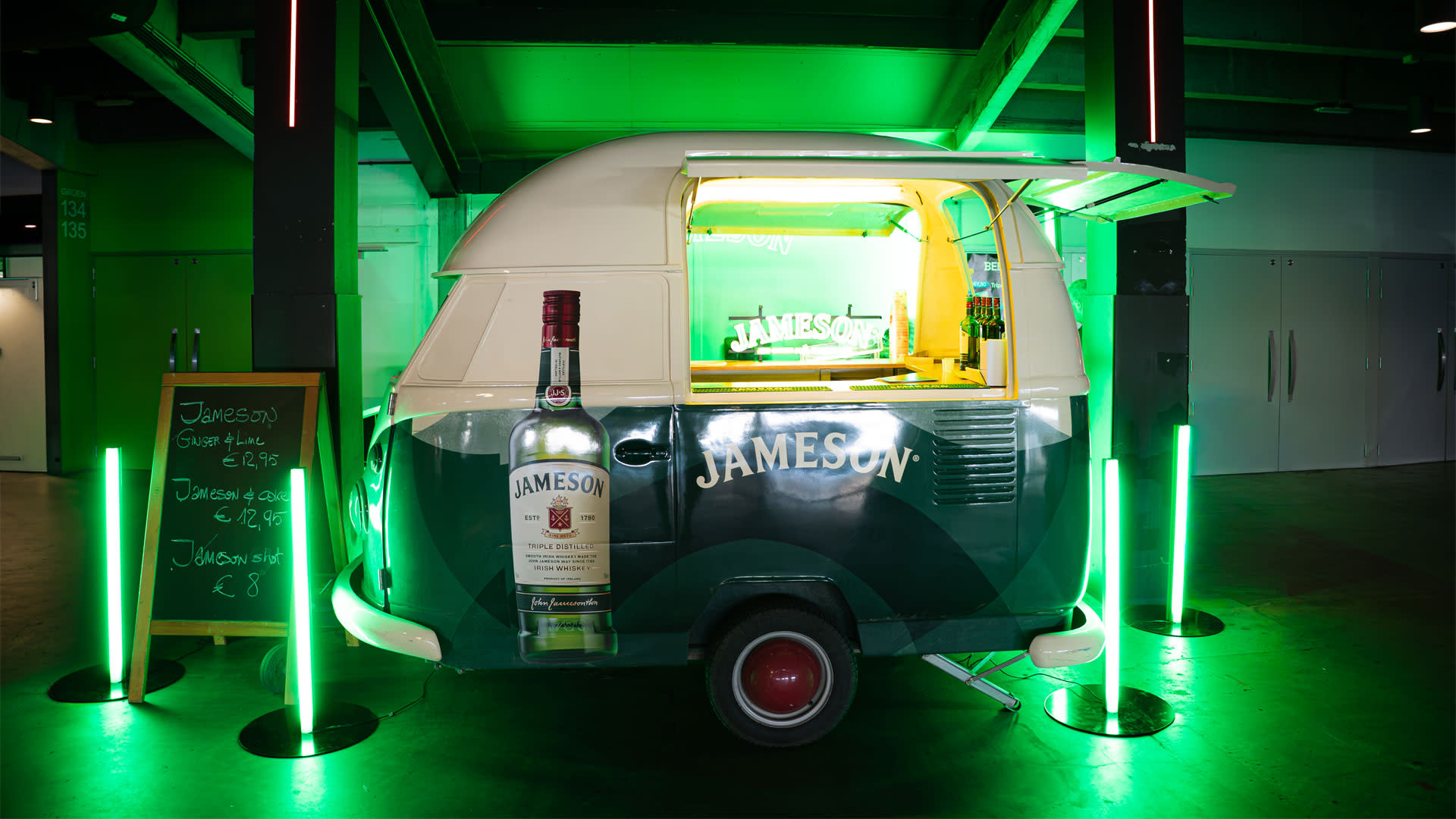 Stand d'activation Jameson à l'AFAS Dome lors d'un concert de rock, avec un bar mobile aux couleurs de la marque, un éclairage vert immersif et une expérience de marque conçue pour attirer les visiteurs.