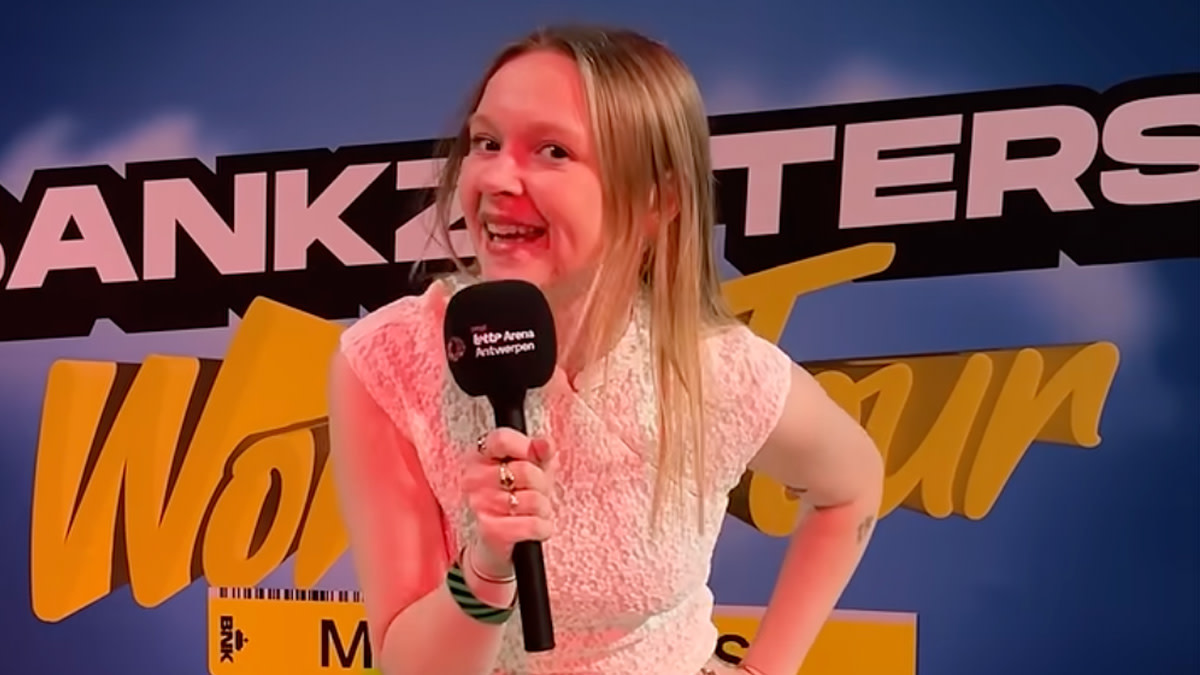 Maike met microfoon staat voor een Bankzitters-achtergrond op zoek naar de grootste fan.