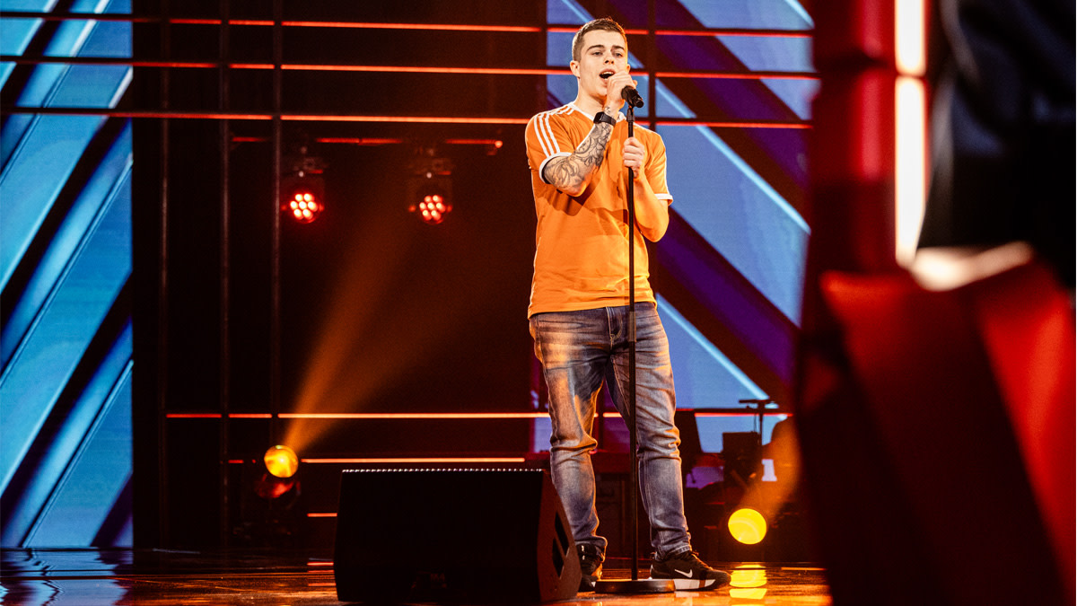 Aron Rademakers in een oranje t-shirt op het podium van The Voice.