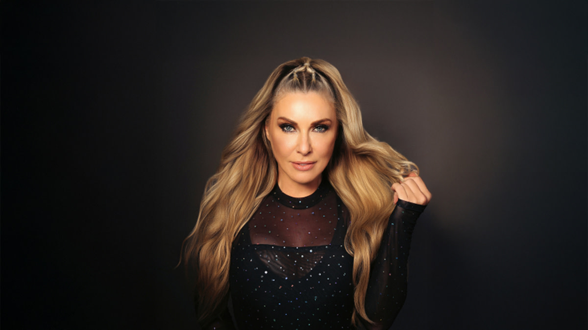 Zangeres Jessy De Smet met lang blond haar en een zwarte outfit tegen een zwarte achtergrond.