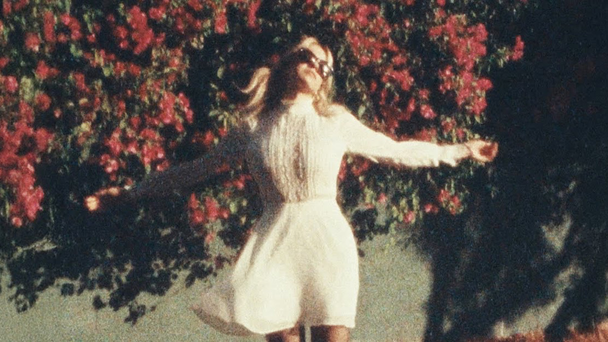 Zangeres Paige Turner van Sunday (1994) in een witte jurk voor een haag van rode bloemetjes.