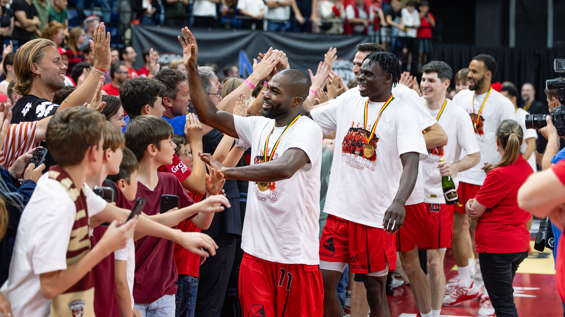 Spelers van Windrose Giants Antwerp geven supporters high-fives na een wedstrijd, omringd door fans in de tribunes.