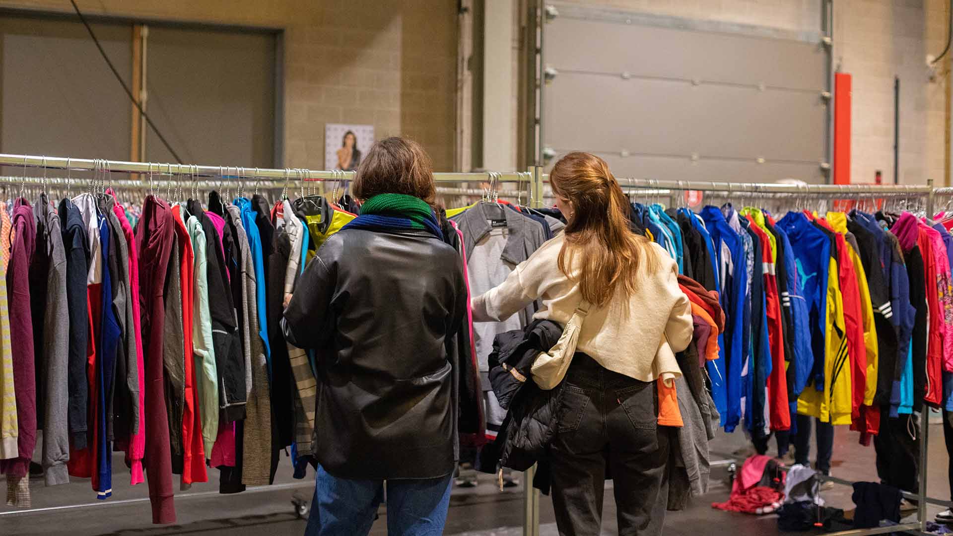 Twee vrouwen snuisteren door een rek met vintage kleding.