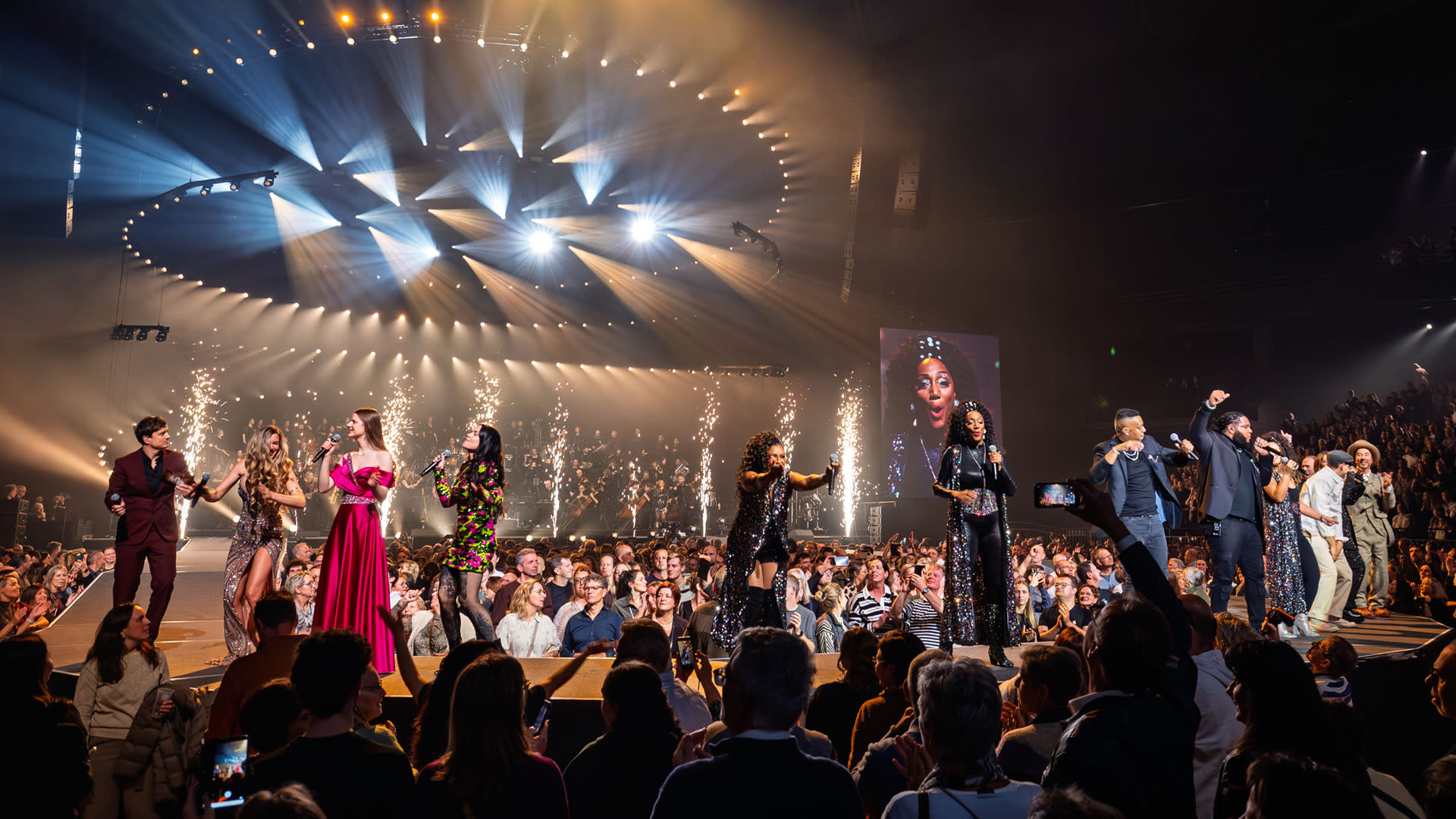 Artiesten op de catwalk tijdens de jubileumeditie van Night of the Proms in een uitbundig verlichte AFAS Dome.