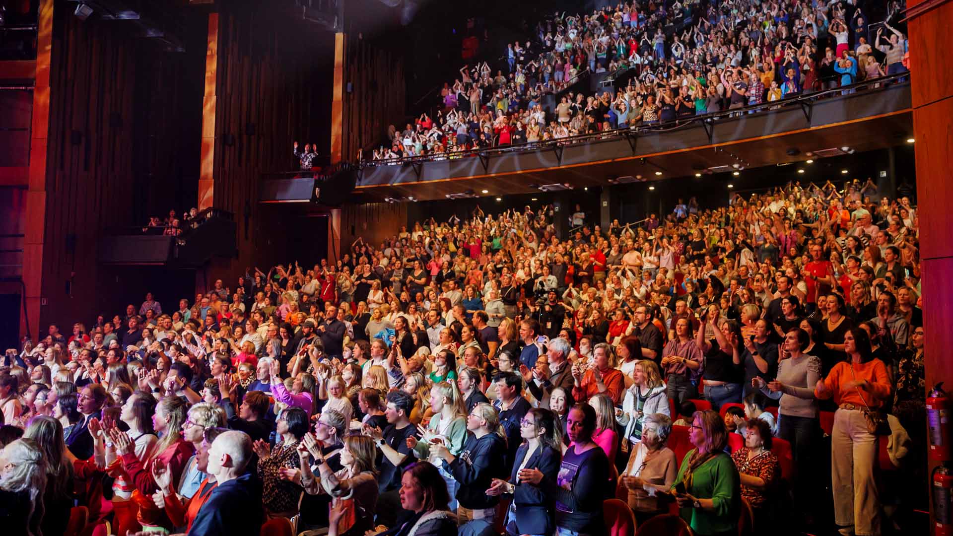 The audience on the floor and in the balcony is standing and applauding.