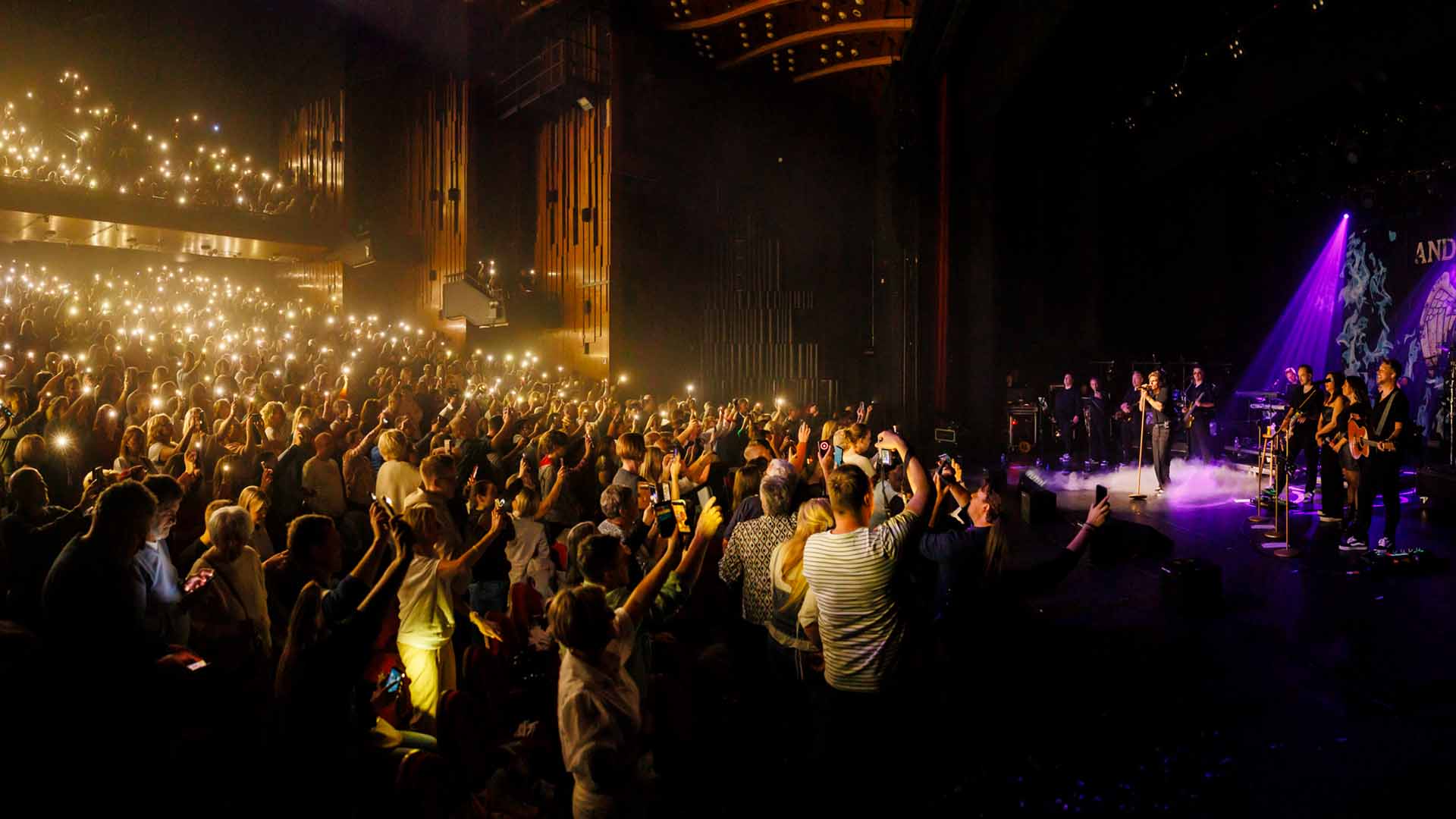André Hazes and his band are on stage. People in the audience are standing and holding up lights.
