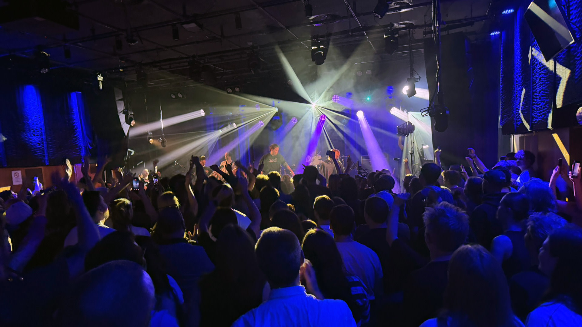 Fans met opgestoken armen kijken naar Nothing But Thieves op het podium van de AB Club, onder paarse en witte lichtstralen.