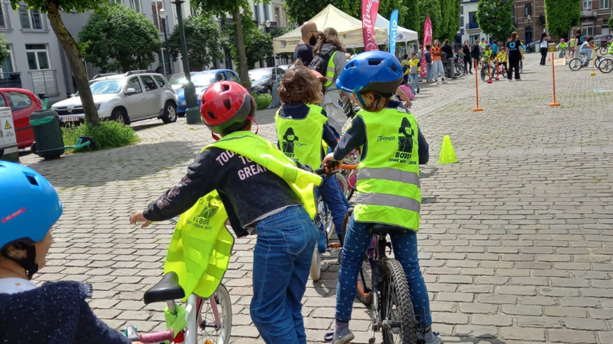 Kinderen fietsen op een behendigheidsparcours tijdens een Vollenbike-activiteit in de openlucht, begeleid door vrijwilligers in fluohesjes.