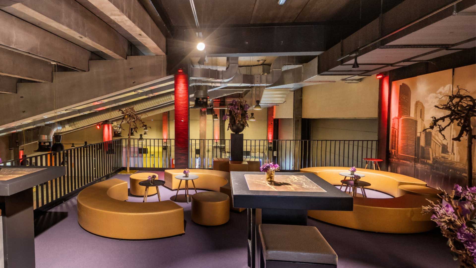Intérieur d’une loge au Trixxo Theater Hasselt avec des banquettes arrondies, des tables, un éclairage d’ambiance et une vue sur le foyer situé en contrebas.”