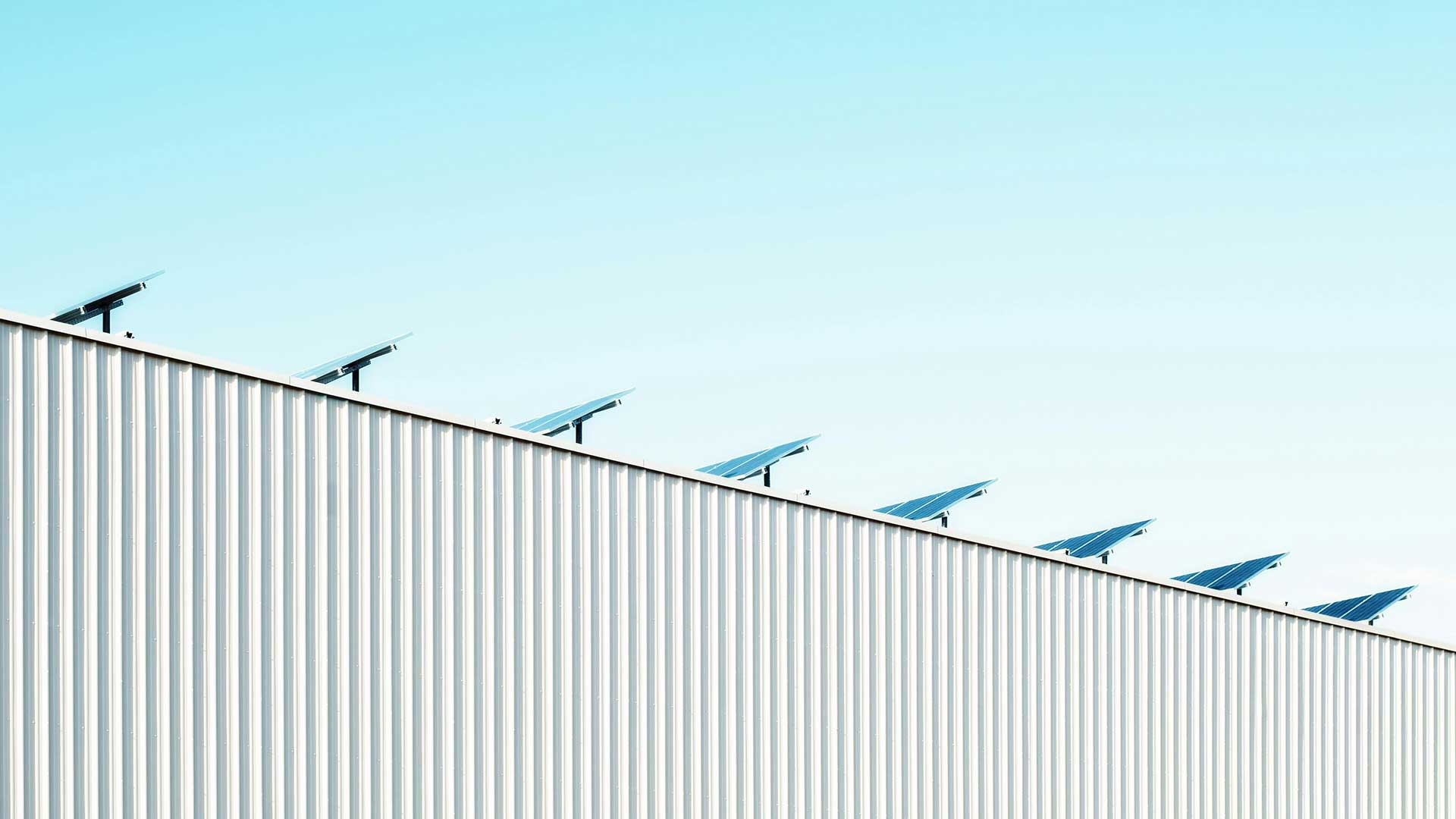Solar panels on a gently sloping metal roof beneath a clear blue sky, creating a clean, minimalist composition.