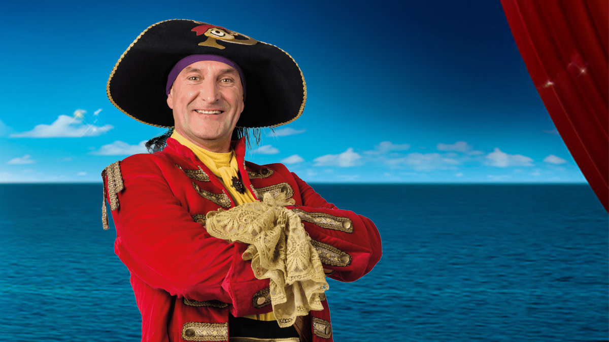 Piet Piraat staat met de armen gekruist centraal in beeld met op de achtergrond een blauwe zee en lucht.