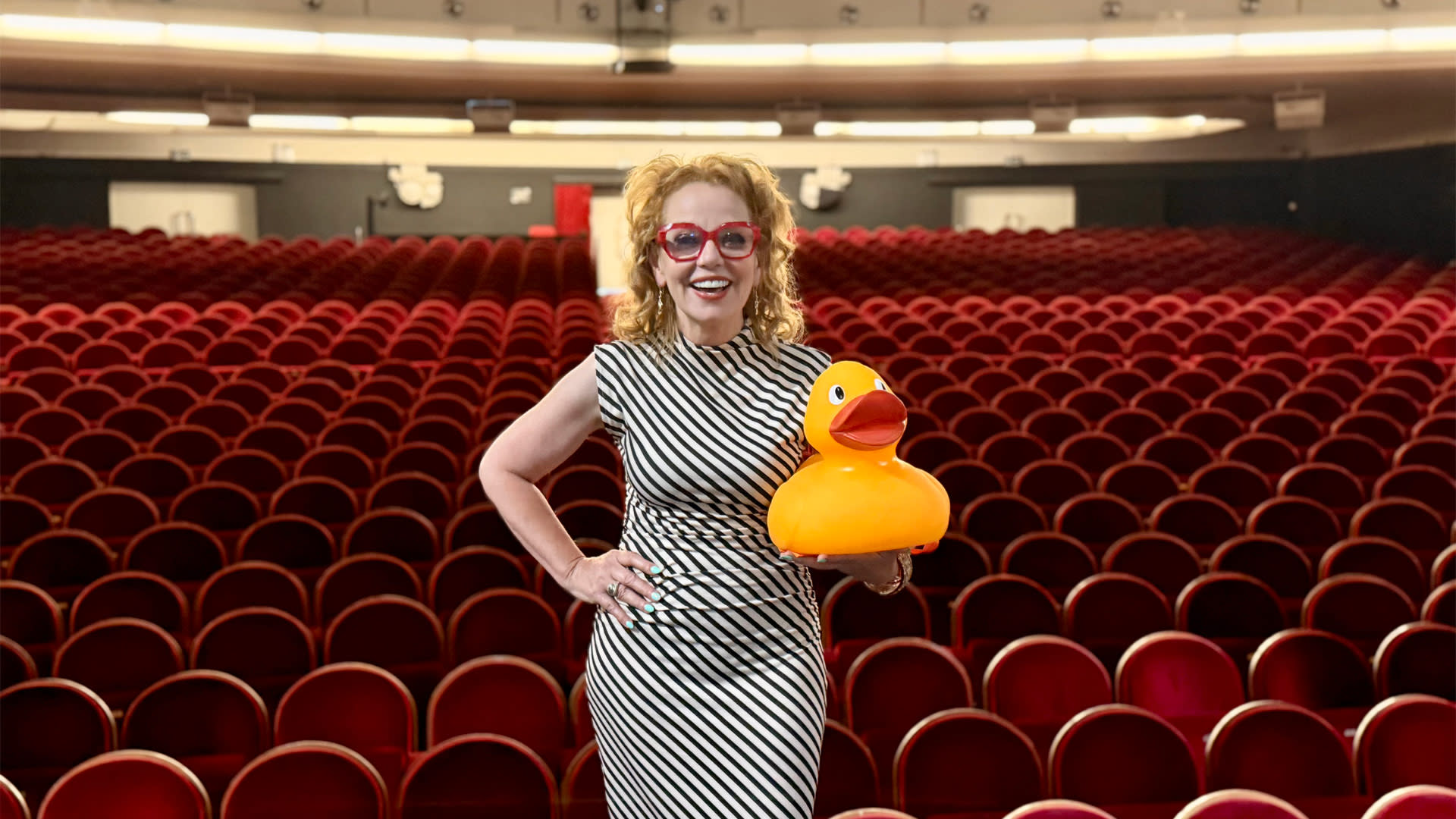 Comedienne Els De Schepper staat met een gele badeend in de hand op het podium in Capitole Gent, met haar rug naar die typische rode theaterstoelen.