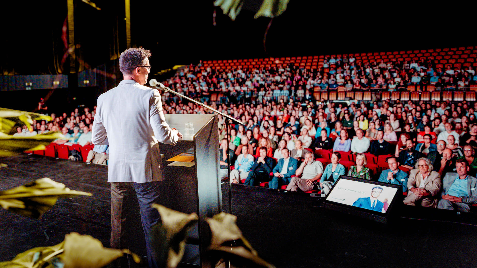 Speaker on stage during a PXL University College event at the Trixxo Theater, with a full audience in the background.