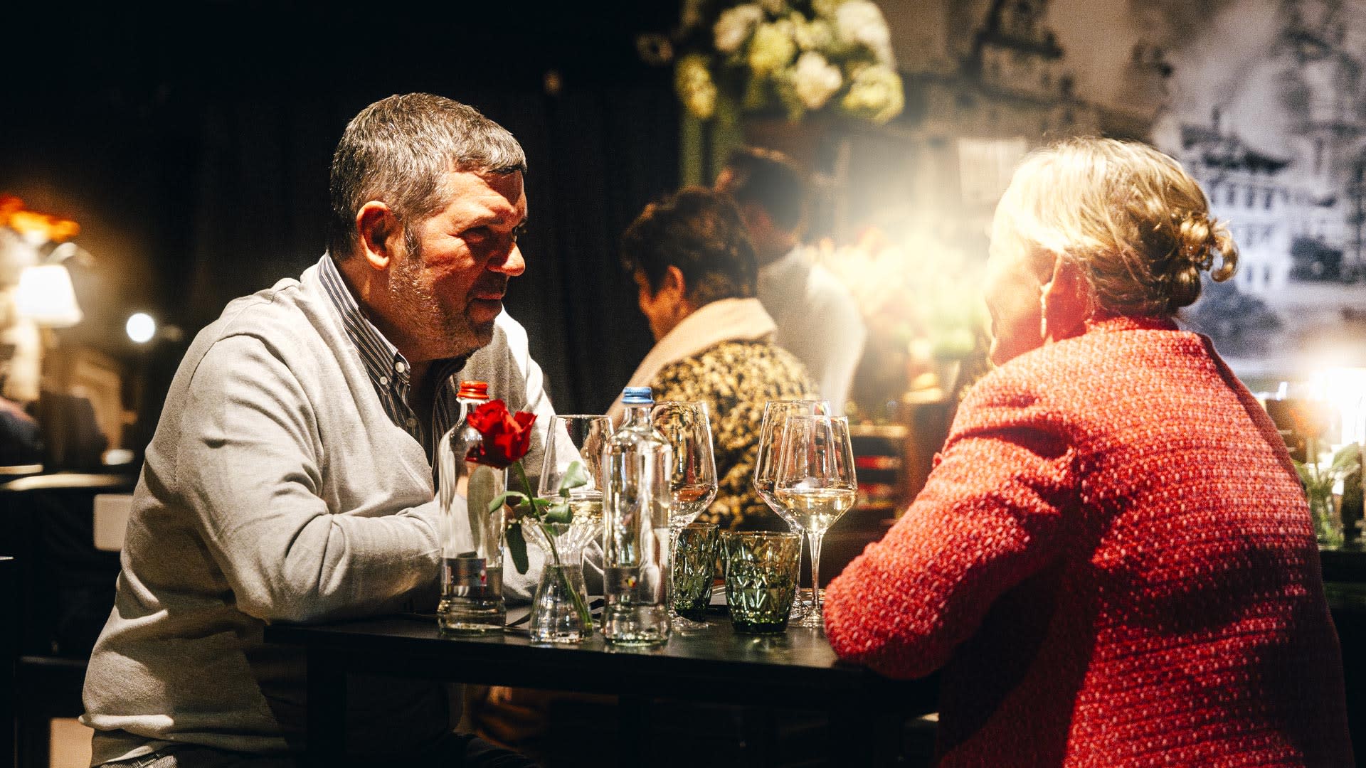Twee gasten genieten van een VIP-ervaring aan een sfeervol gedekte tafel met wijn en water in een warme, intieme setting.