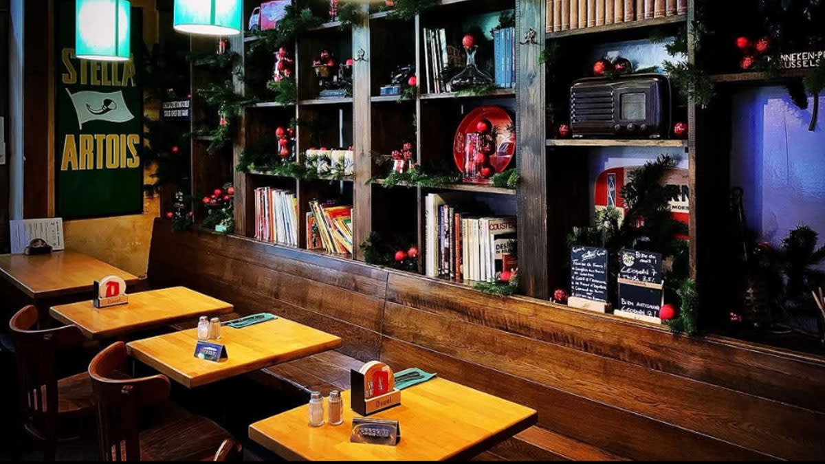 Intérieur chaleureux du restaurant Schieve Lavabo à Forest, avec des tables en bois, des étagères remplies de livres et des décorations festives.