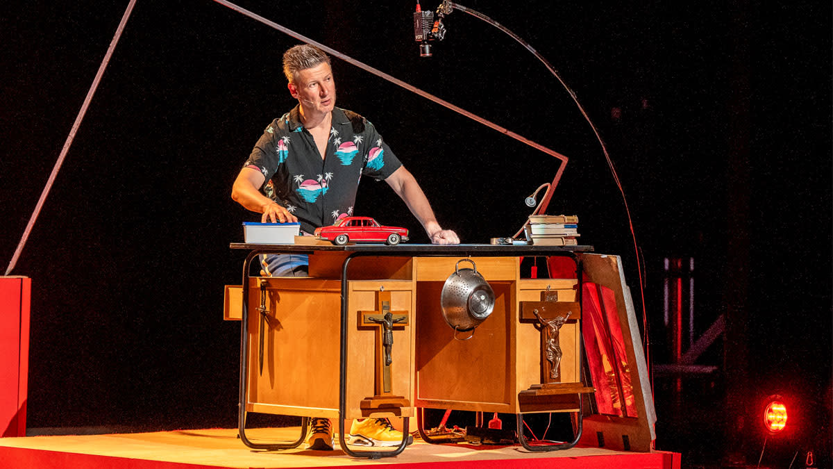 Wouter Deprez staat op het podium achter zijn rommelig bureau.
