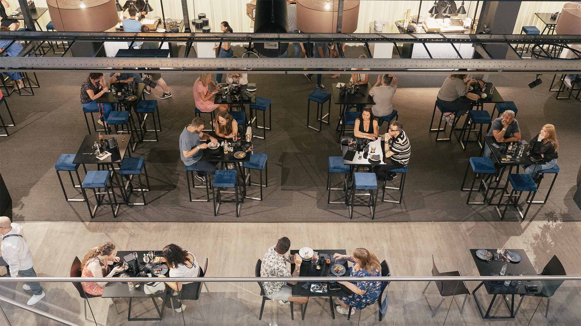 Een bovenaanzicht van het Hospitality Center waar gasten genieten van maaltijden aan verschillende tafels met blauwe stoelen.