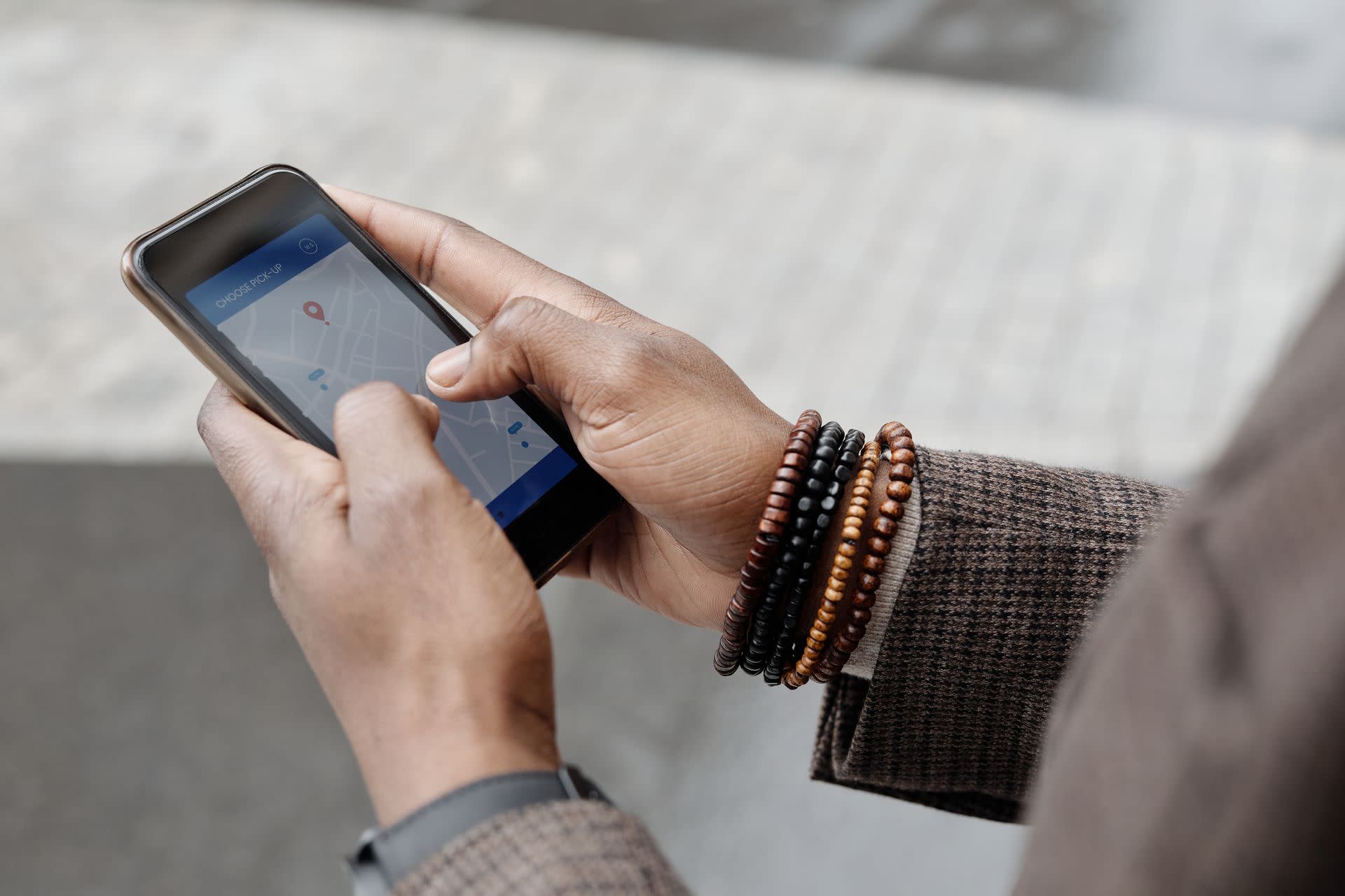 Handen van een persoon die een smartphone vasthoudt met een kaart- of navigatieapp zichtbaar op het scherm, terwijl de persoon buiten op straat staat.