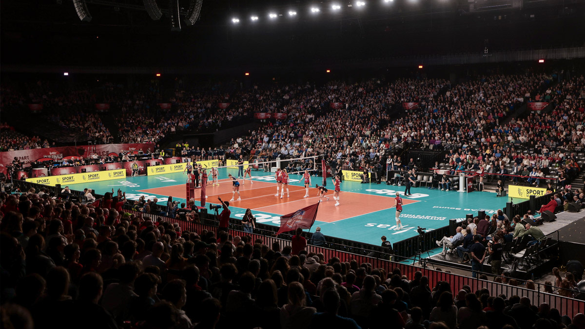 Een volle AFAS Dome tijdens een volleybalwedstrijd, met twee teams op het veld en duizenden toeschouwers die rondom de arena intens meeleven met het spel.