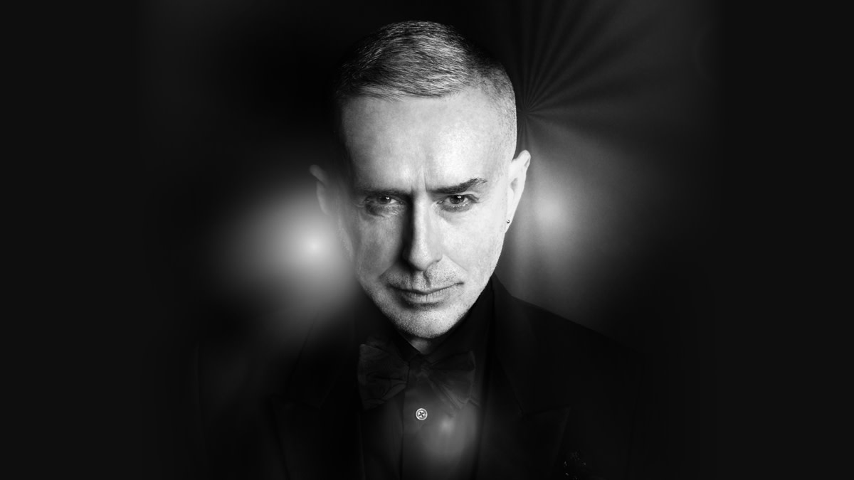 Portret van Holly Johnson tegen een lichte achtergrond. De Britse zanger kijkt recht in de camera en is afgebeeld in een zwart hemd. Zijn portret wordt omgeven door een organische turquoise vorm met een zachte, dromerige gloed.