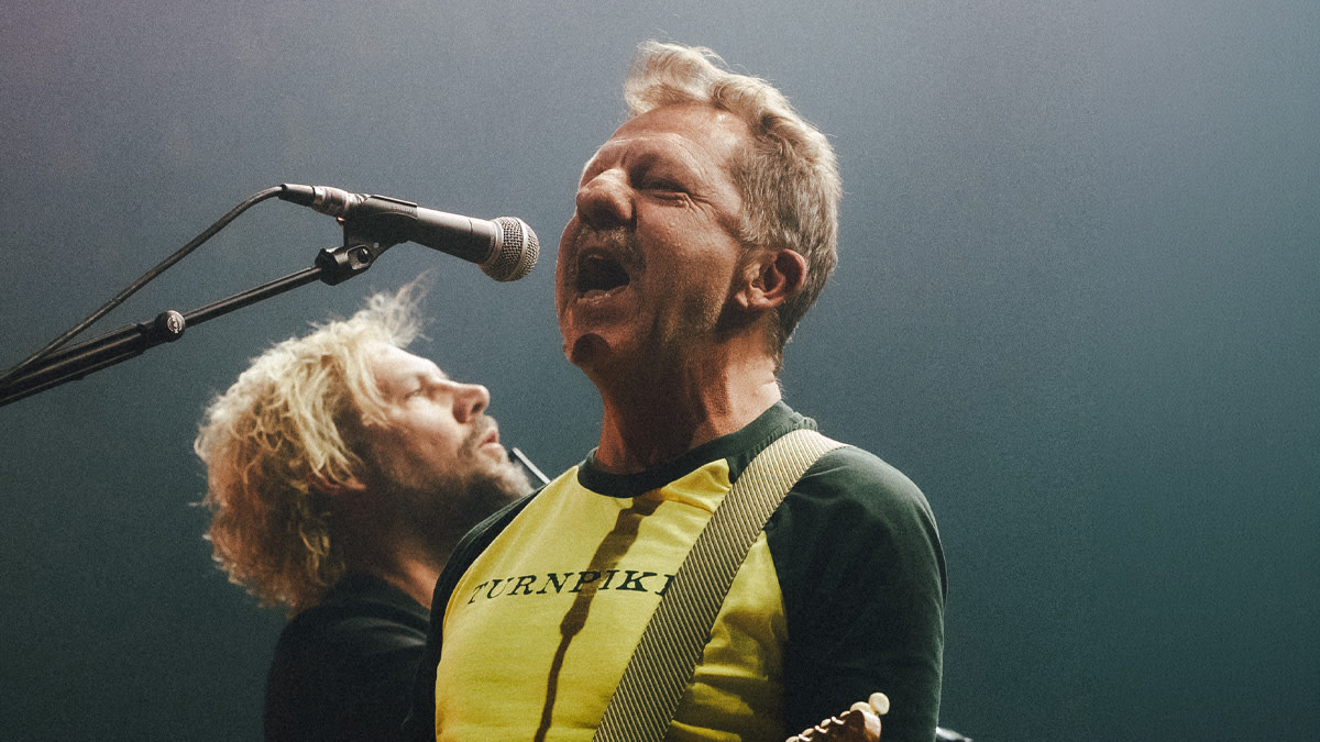 Tom Barman - frontman van dEUS - gele t-shirt zingend voor een microfoon.