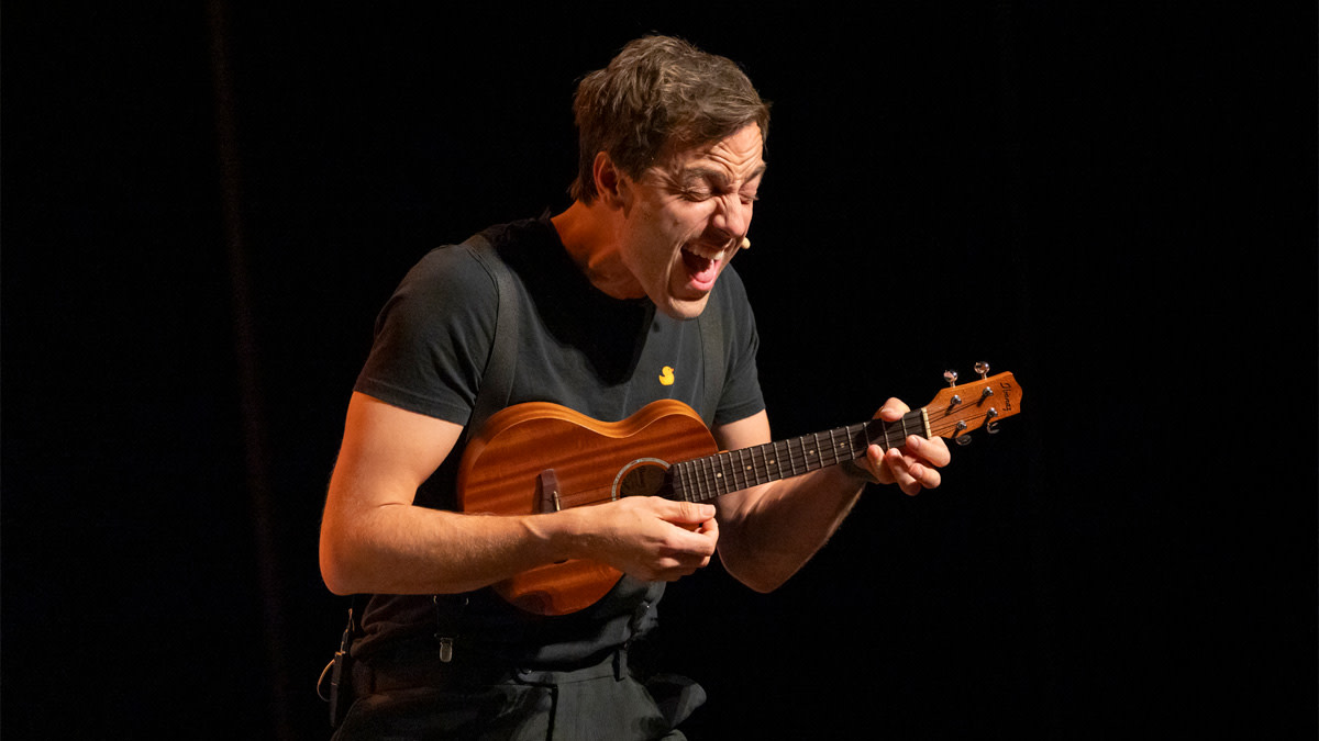 Guga Baul met in z'n hand een kleine gitaar staat tegen een zwarte achtergrond. Hij is één van de artiesten die deze week werden aangekondigd in onze theaters.