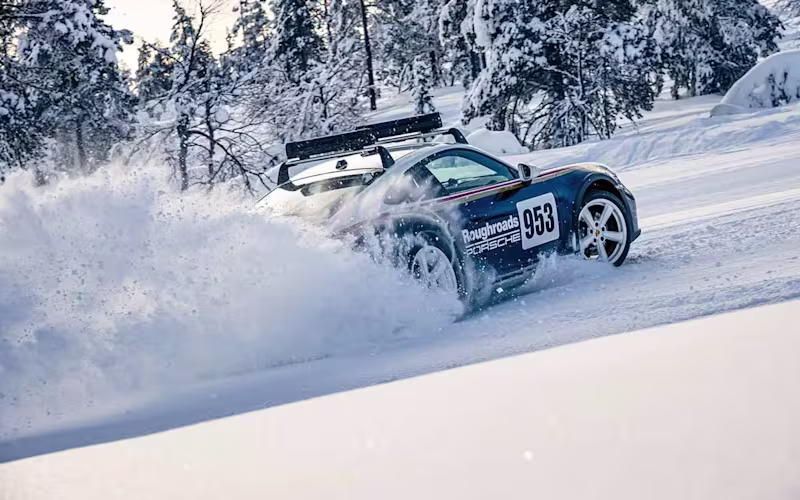 Porsche 911 Dakar drifts on snow, pine tree forest in the background.