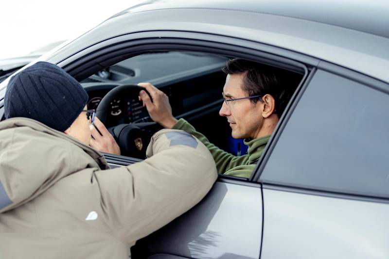Instructor leans into window giving instructions to a driver in a Porsche.