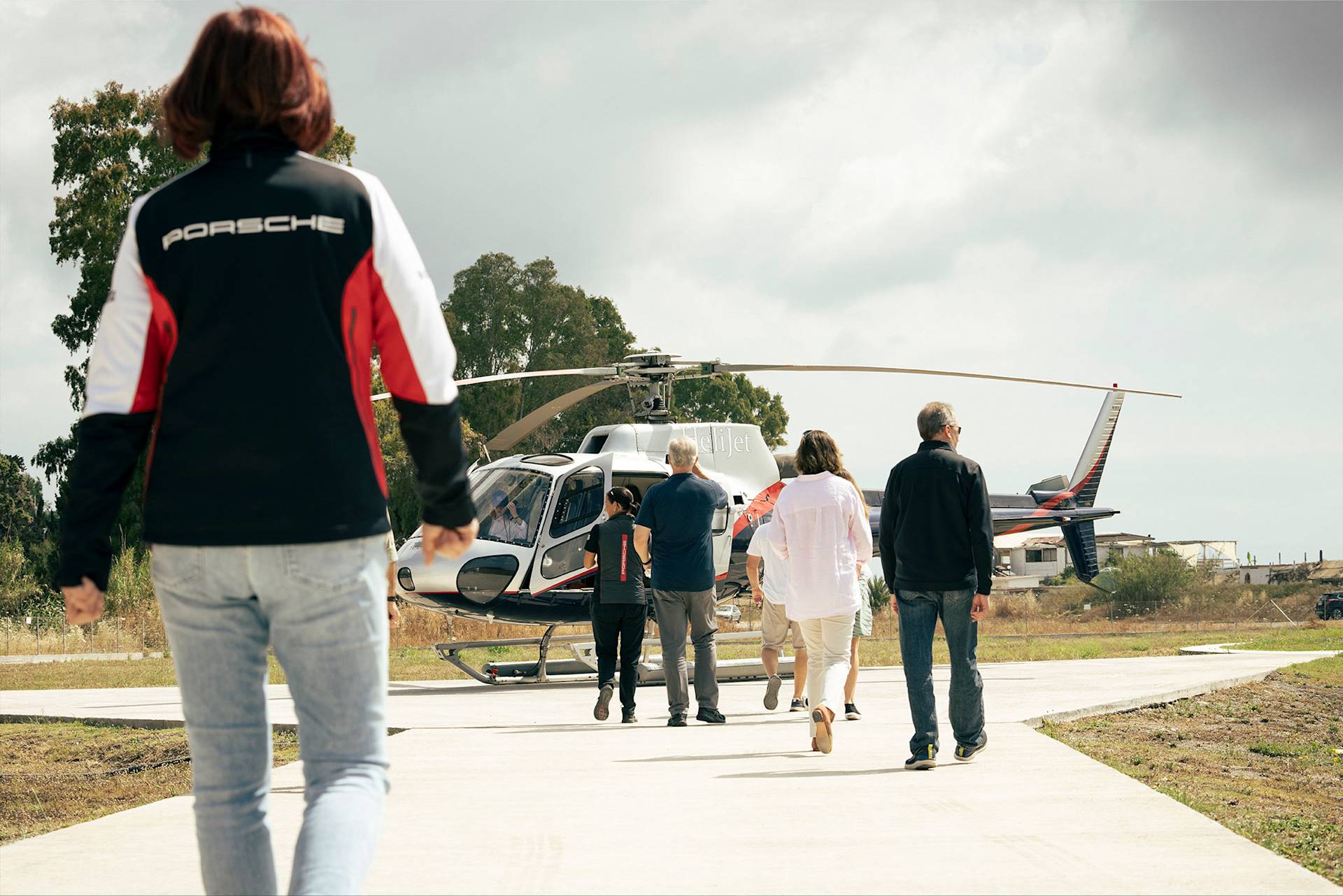 Five people walking towards a helicopter on a cloudy day.