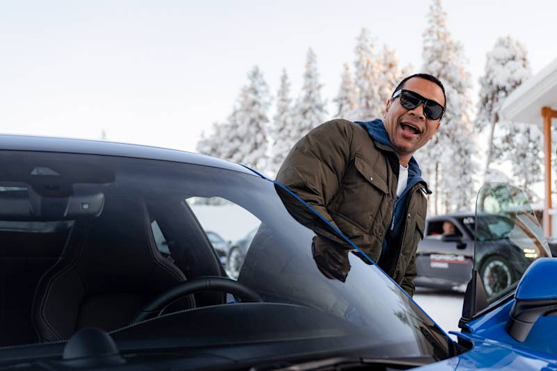 A man is smiling while getting into a blue Porsche in a snowy setting during the Porsche Ice Experience.