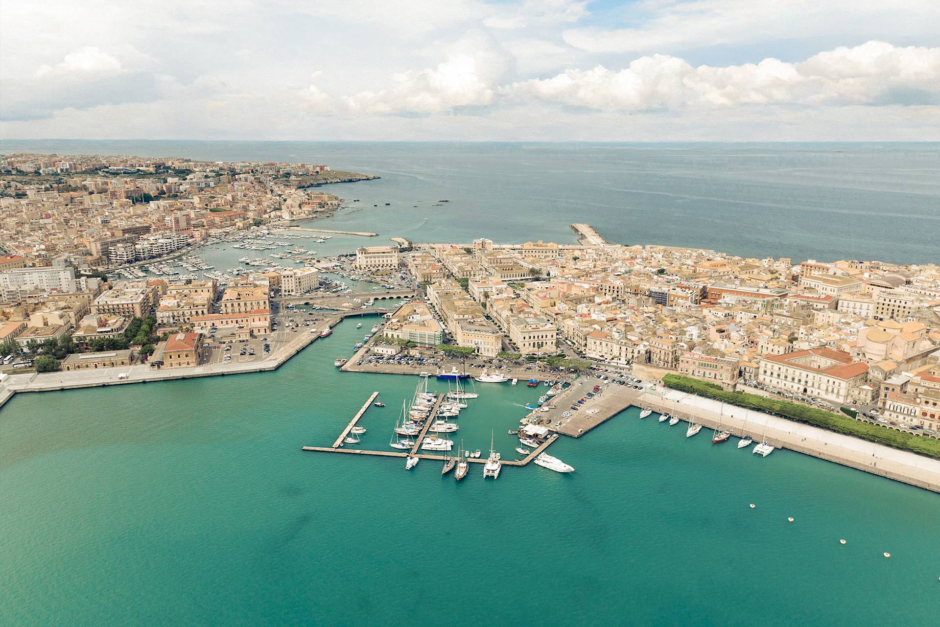 Aerial view of coastal city with marina, docks, and turquoise water near historic areas.