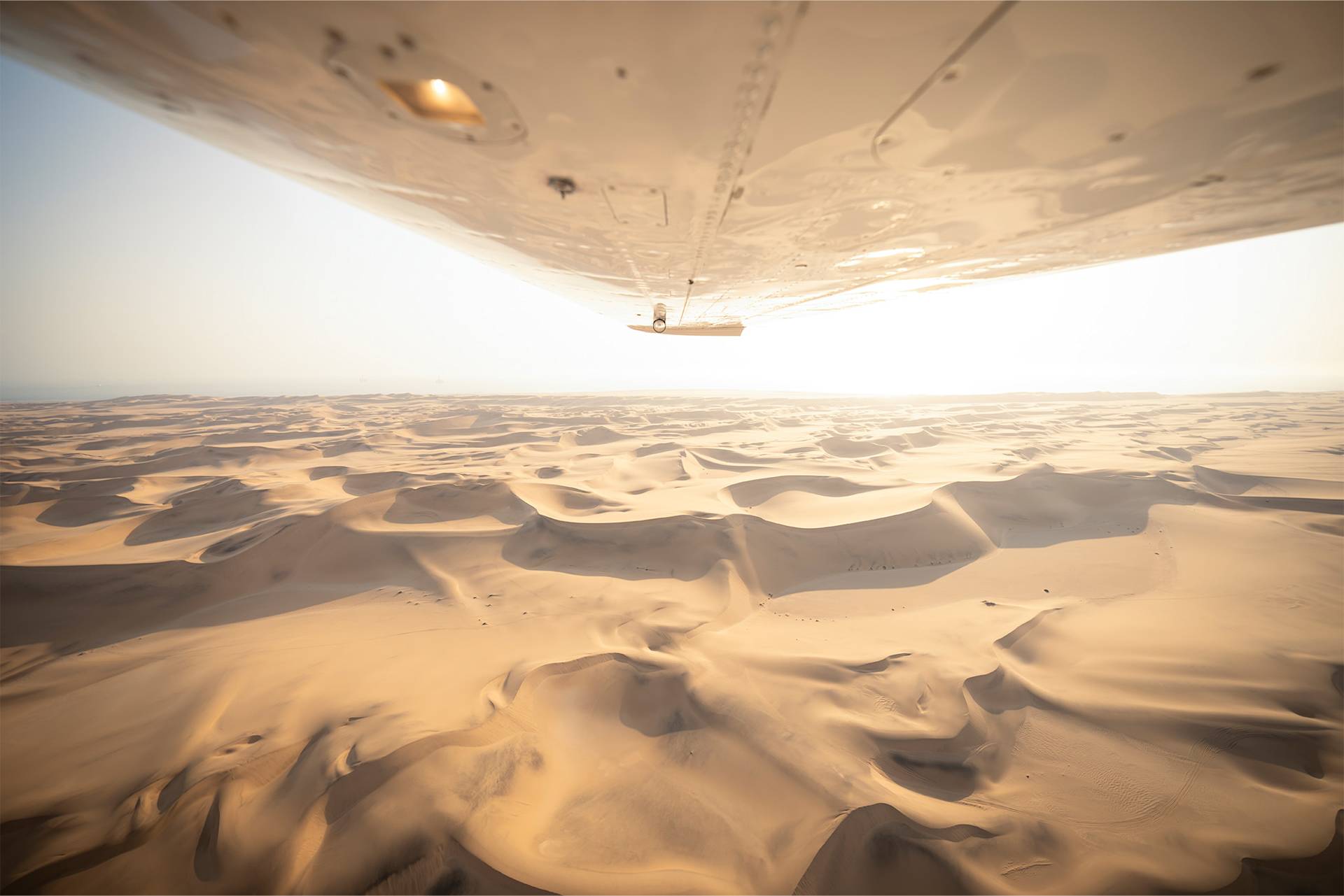 Aerial shot of sunrise over desert dunes with airplane wing visible.
