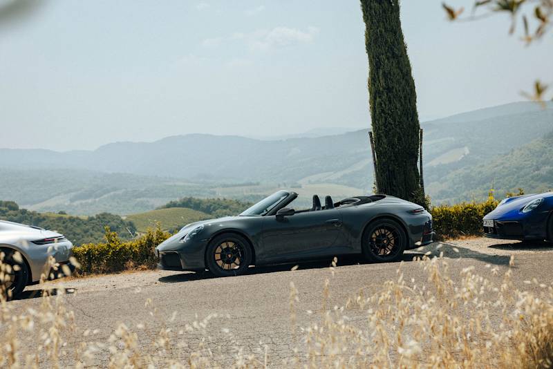 Schwarzer Porsche Cabrio parkt an malerischer Straße mit Hügeln.