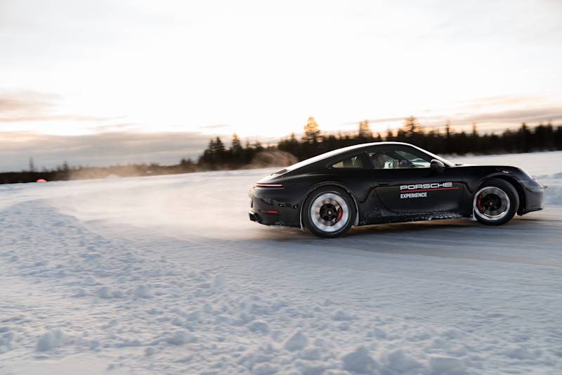 Black Porsche 911 drifting dynamically across the icy track at sunset.